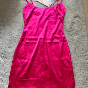 Rosa klänning med smala axelband - Snygg rosa klänning med smala axelband i ett glansigt material. Perfekt för en kväll ute eller en speciell tillställning. Tillverkad i 92% polyester och 8% spandex för en bekväm passform.