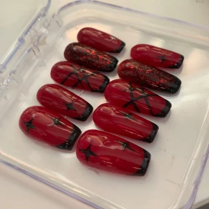 Röda gelenaglar med svarta detaljer - Snygga röda lösnaglar med svarta spetsar och stjärndetaljer. Perfekta för en dramatisk look med en touch av glitter. Kommer i en praktisk förpackning. Allt som behövs för att sätta fast dem följer med!
