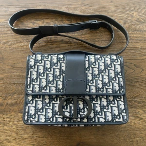 Mönstrad axelväska  - Snygg axelväska  med ett ikoniskt mönster i svart och vitt. Väskan har en justerbar axelrem och ett elegant spänne framtill. Perfekt för att ge din outfit en lyxig touch. 