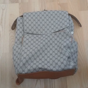 Mönstrad ryggsäck från Don Donna - Snygg ryggsäck från Don Donna med ett stilrent mönster i grått och brunt. Väskan har justerbara axelremmar och flera praktiska fack med dragkedja. Perfekt för att bära med sig allt man behöver under dagen.