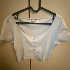 Ljusblå kortärmad topp från 157 - Säljer en söt ljusblå topp från 157 med korta ärmar och knappar framtill. Perfekt för en avslappnad stil. Toppen har en v-ringad design som ger en feminin touch.