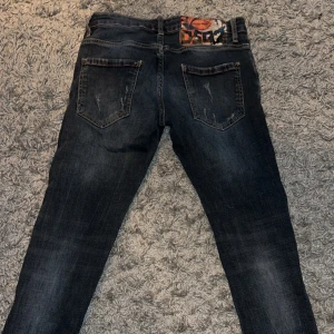 Blå jeans med slitningar - Säljer ett par blåa jeans med coola slitningar och en unik patchdetalj på bakfickan. Jeansen har en slim passform och är perfekta för en trendig look. De har både dragkedja och knappar framtill. Köpa här på plick av en seriös grabb för 3400kr 