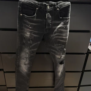Svarta jeans från Dsquared2 - Snygga svarta jeans från Dsquared2 med slitna detaljer och färg stänk som ger en cool look. De har en klassisk femficksdesign och en knappgylf. Perfekta för dig som vill ha en edgy stil.