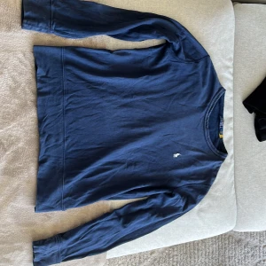 Blå långärmad tröja från Ralph Lauren - Säljer en stilren marinblå långärmad tröja från Ralph Lauren med det klassiska broderade logotypen på bröstet. Perfekt för en avslappnad och snygg look. Tröjan har en rund halsringning och är tillverkad i 100% bomull. Nypris 1600kr mitt pris 350kr. Skick 9/10 inga defekter alls. Skriv om frågor eller mer bilder🤩🙌