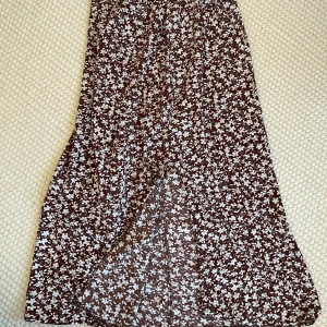 Brun blommig långkjol - Brun långkjol med ett sött blommönster i vitt. Har en liten slits nertill