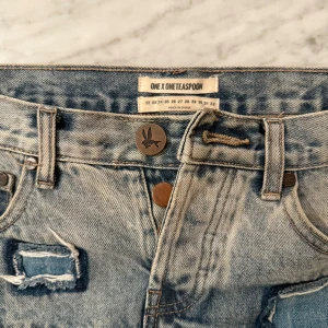 Jeanskjol från One Teaspoon - Trendig jeanskjol från One Teaspoon med en unik design. Kjolen har lappdetaljer och en dekorativ stjärna på framsidan. Fickor finns både fram och bak. Färgerna är en blandning av olika nyanser av denim. Nypris 1700kr.