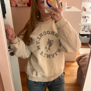 Beige sweatshirt med tryck - Säljer en beige sweatshirt med ett coolt tryck av en basketspelare. Tröjan har långa ärmar och en avslappnad passform, perfekt för en casual look. Passar bra till jeans.