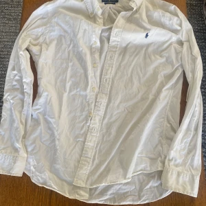 Vit skjorta från Ralph Lauren - Säljer en klassisk vit skjorta från Ralph Lauren i slim fit. Skjortan är tillverkad i lätt twill och har långa ärmar med knappar framtill. Den har en broderad logotyp på bröstet. Säljer för den är för stor för mig. Enda med den är nästan osynliga deo fläckar som inte syns när den e på. 
