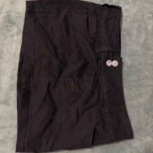 Svart minikjol med fickor  - Snygg svart minikjol med praktiska fickor och knappdetaljer framtill. Perfekt för fester och annat.