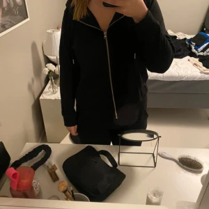 Svart hoodie från H&M - Säljer en klassisk svart hoodie från H&M med dragkedja och huva. Perfekt för en avslappnad stil. Den har långa ärmar och dragsko vid huvan för justerbar passform.