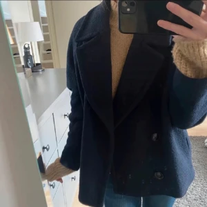 Mörkblå kappa - Snygg mörkblå kappa med dubbelknäppning och bred krage. Perfekt för kyligare dagar. Passar bra över en stickad tröja för extra värme. Storlek 34/36 