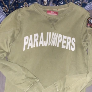  fleece tröja från Parajumpers storlek 164 - Säljer en olivgrön fleece tröja från Parajumpers med stort vitt tryck på framsidan och ett snyggt märke på ärmen. Perfekt för kyliga dagar och ger en cool look. Passar bra till jeans eller joggers. Storlek 158-164 