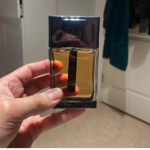 Dior Homme Intense Parfym - Säljer en elegant Dior Homme Intense parfym i en stilren glasflaska med svart lock. Doften är intensiv och maskulin, perfekt för den som vill göra ett intryck. Flaskan har en modern design med en tydlig etikett framtill.