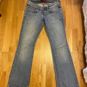 Blå bootcut jeans med low waist - Snygga blå bootcut jeans med klassisk femficksdesign och knappgylf. Perfekta för en avslappnad stil. De har en lätt tvättad look som ger en vintage känsla.