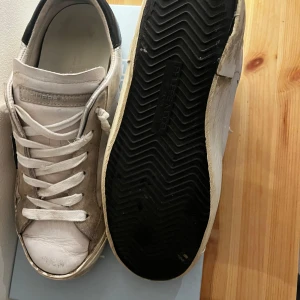 Vita sneakers från Philippe Model - Snygga vita sneakers från Philippe Model med svarta detaljer och snörning och slitningar som är en del av designen. Skorna har en klassisk design med en bekväm passform och är perfekta för en stilren look. (Pris kan diskuteras)