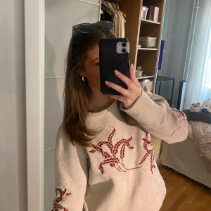 Beige tröja med broderi - Säljer en beige tröja med unik röd broderad design på framsidan och ärmarna. Tröjan har långa ärmar och en avslappnad passform. Perfekt för en stilren och bekväm look. Lite tunnare så perfekt nu till våren och sommaren Priset kan diskuteras 💞❤️