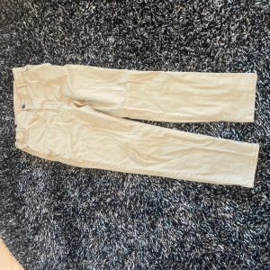 Beige chinos från H&M - Snygga beige chinos från H&M med en klassisk design. Byxorna har en knapp och dragkedja framtill samt fickor både fram och bak. Perfekta för en stilren look.