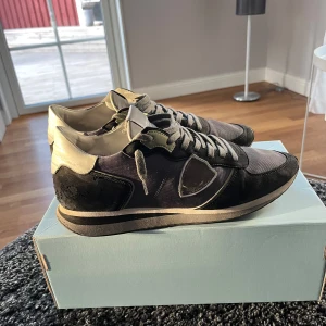 Svarta sneakers från Philippe Model - Snygga svarta sneakers från Philippe Model med grå och vita detaljer. Skorna har en klassisk design med snörning och en bekväm sula. Perfekta för en stilren och avslappnad stil nu till våren. Riktigt bra skick och box ingår vid snabb affär. 