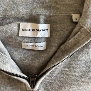 Grå merinoulltröja från These Glory Days - Säljer en stilren grå tröja i merinoull från These Glory Days. Tröjan har en dragkedja vid halsen och korta ärmar, perfekt för lager-på-lager eller som den är. Den mjuka merinoullen ger en lyxig känsla och håller dig varm. (Sitter mer som storlek S)