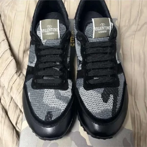 Valentino Garavani sneakers i svart och grått - Snygga Valentino Garavani sneakers med ett coolt camouflagemönster i svart och grått. Skorna har snörning och en unik design med nitar på hälen. Perfekta för att ge din outfit en edgy touch.