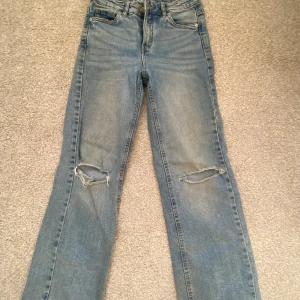 Blå jeans från LAB Industries - Säljer ett par blå jeans från LAB Industries med slitna detaljer på knäna. De har en klassisk femficksdesign och knappgylf. Perfekta för en avslappnad stil.