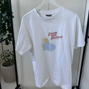 Vit t-shirt med tryck från Jacquemus - Säljer en vit t-shirt från Jacquemus med ett färgglatt tryck och texten 'Bonne nuit Jacques'. Perfekt för en avslappnad stil. T-shirten har en klassisk rund hals och korta ärmar.