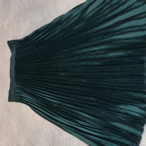 Grön plisserad kjol  st S - Snygg grön plisserad kjol i ett glansigt material. Perfekt för att ge en elegant touch till din outfit. Kjolen har en elastisk midja för bekväm passform.