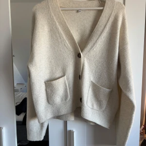 Beige kofta med knappar - Mysig beige kofta med v-ringning och knappar framtill. Den har två praktiska fickor och ribbade kanter. Perfekt för kyliga dagar.