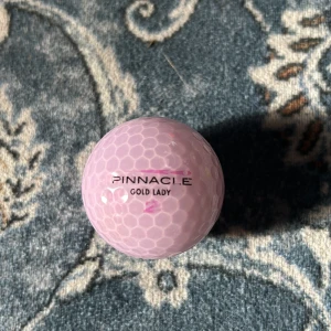 Ljuslila golfboll från Pinnacle - Säljer en ljuslila golfboll från Pinnacle, modell Gold Lady. Perfekt för golfentusiaster som vill ha en unik färg på banan. Bollen har en klassisk dimple-design för optimal flygprestanda.