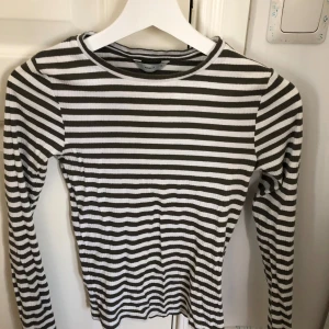 Randig långärmad tröja från Pigalle - Säljer en stilren randig tröja från Pigalle i grön och vit. Tröjan har långa ärmar och en rund halsringning, perfekt för en avslappnad look. Passar bra till jeans eller kjol!