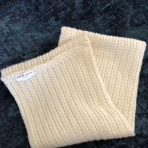 Beige stickad halsduk från Zara - Säljer en mysig beige stickad halsduk från Zara. Den är ribbstickad och perfekt för att hålla dig varm under kyliga dagar. En stilren accessoar som passar till många olika outfits.