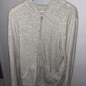 Grå kashmir hoodie från John Henric - Säljer en stilren grå kashmir hoodie full zip från John Henric. Tröjan har dragkedja framtill och en bekväm huva. Perfekt för en avslappnad outfit. 100% Kashmir!