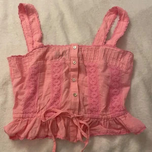 Rosa topp med spetsdetaljer från Sportsgirl - Söt rosa topp från Sportsgirl med spetsdetaljer och knappar framtill. Toppen har breda axelband och en volangkant nedtill. Perfekt för en somrig look! 💖motsvarar ca storlek xxs/xs 