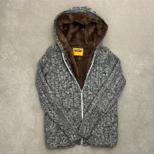 Fodrad Päls Cardigan  - Mysig grå stickad jacka från Gildan med brun fuskpälsfoder. Jackan har en dragkedja framtill och en huva för extra värme. Perfekt för kyliga dagar. Vid minsta fråga eller fundering hör av er🤝