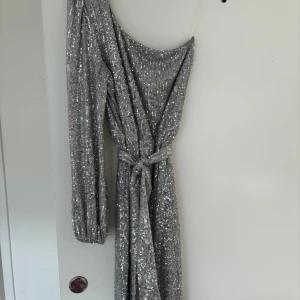 Silver glittrig oneshoulder klänning - En fantastisk klänning. Som en liten disco kula 🙏🏻 one shoulder. Slutar vid ankeln på mig  Den är i väldigt fint skick. Använd vid 1 tillfälle Dock så fastnar paljetterna i varandra och därför kan det vara lite paljetter som skavts av. Dock går det tyvärr inte att undvika med denna klänningen då den är helt täckt i paljetter  Bilden gör den inte rättvisa! Den är otrolig i verkligheten 🪩