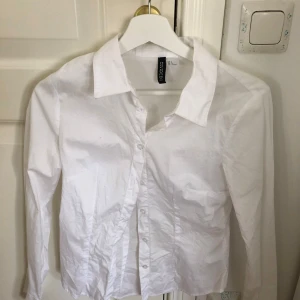 Vit skjorta från H&M - Säljer en klassisk vit skjorta från H&M i storlek M. Skjortan har långa ärmar och knappar framtill. Perfekt för en stilren look.