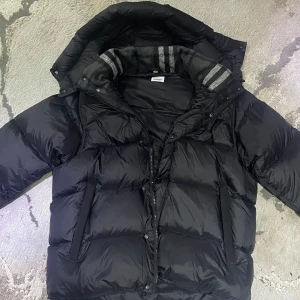 Svart dunjacka från Burberry - Säljer en stilren svart dunjacka från Burberry.  Den kan bli till en väst perfekt till våren/sommarnen. Jackan har en quiltad design med långärmade ärmar och en praktisk dragkedja framtill. Perfekt för kyliga dagar med sin varma och bekväma passform.