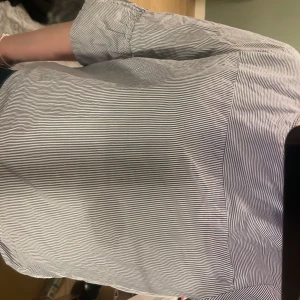 Randig skjorta från Tommy Hilfiger - Säljer en stilren blå- och vitrandig skjorta från Tommy Hilfiger. Skjortan har långa ärmar och knappar baktill dock har en av knapparna gått av. Har även en fett fläck som inte är så synlig. *köpare står för frakt*