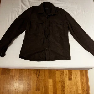 Brun overshirt från Dressmann - Säljer en stilren brun overshirt från Dressmann. Jackan två bröstfickor med lock. Perfekt för lager-på-lager under kyligare dagar.