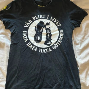 Svart t-shirt från Black Army Design (UN) - Svart t-shirt med tryck fram och bak. Framsidan har texten 'Vår plikt i livet Hata Hata Hata Göteborg' och en bild av kängor. Baksidan har texten 'ACAB'. Perfekt för dig som har rätt prioriteringar i livet.
