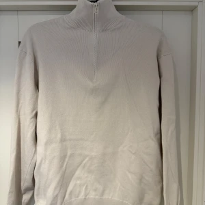 Beige tröja med dragkedja från Zara - Säljer en stilren beige tröja från Zara med halv dragkedja och hög krage. Perfekt för en avslappnad och snygg look. Tröjan har långa ärmar och är tillverkad i ett mjukt material.