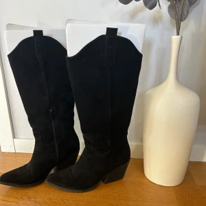 Svarta cowboy boots i mocka - Snygga svarta cowboy boots i mocka med spetsig tå och klack. Perfekta för en stilren look med en touch av vilda västern. De har en dragkedja på insidan för enkel på- och avtagning.🩷 säljer då dom inte längre kommer till användning, en liten defekt på ena tån