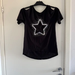 Svart topp med stjärnmönster - Snygg svart topp med en stor vit stjärna framtill. Toppen har korta ärmar med cut-out detaljer vid axlarna. 