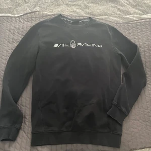 Svart tröja från Sail Racing - Säljer en svart tröja från Sail Racing med vit logotyp på bröstet. Tröjan har långa ärmar och en klassisk rund halsringning. Perfekt för en stilren och sportig look.