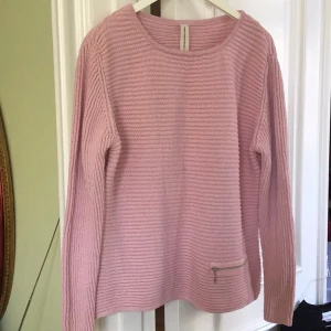 Rosa stickad tröja från Skovhuus - Säljer en söt rosa stickad tröja från Skovhuus i ekologisk bomull. Tröjan har en diskret dragkedja på framsidan och långa ärmar. Perfekt för en mysig dag!