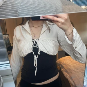Vit croppad blus med knytning - Säljer en vit croppad blus med knytning framtill. Blusen har långa ärmar och en klassisk krage. Perfekt för att lägga till en stilren touch till din outfit.