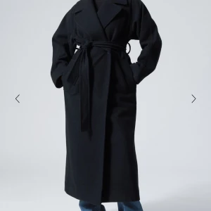 Svart kappa med bälte - Säljer denna svarta lång kappa med knytskärp i midjan. Den har en klassisk design med långa ärmar och en slits baktill. Perfekt för kyligare dagar och nu till våren!! Köpte den här på Plick!!