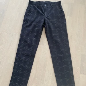 Svarta rutiga byxor från Zara - Snygga svarta byxor från Zara med ett stilrent rutmönster. Byxorna har en klassisk passform och är perfekta för en trendig look. De är tillverkade i ett bekvämt material och har en knappstängning framtill.