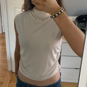 Beige ärmlös topp - Säljer en stilren beige ärmlös topp med hög hals. Perfekt för en minimalistisk look och kan enkelt matchas med olika outfits. Aldrig andvänd! Storlek L men passar mig som oftast bär xs/s. Pris kan diskuteras 