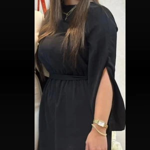 Svart klänning med knytband - Elegant svart klänning med långa ärmar och knytband i midjan. Perfekt för en stilren look.